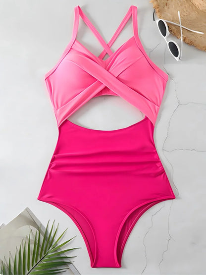Pink one-piece swimsuit on a light gray surface with sunglasses and a palm leaf.