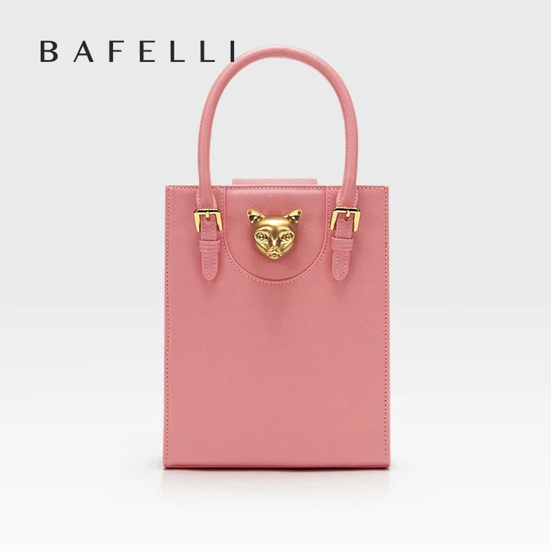 Pink handbag with gold accents on a light gray background, featuring the brand 'Bafelli'. Unisex mini tote crossbody bag in split leather with flap pocket and lock closure. Hard box shape and polyester lining. Casual versatile style.
