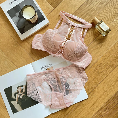 Pink lace lingerie set on a magazine with a candle and perfume bottle on a wooden surface