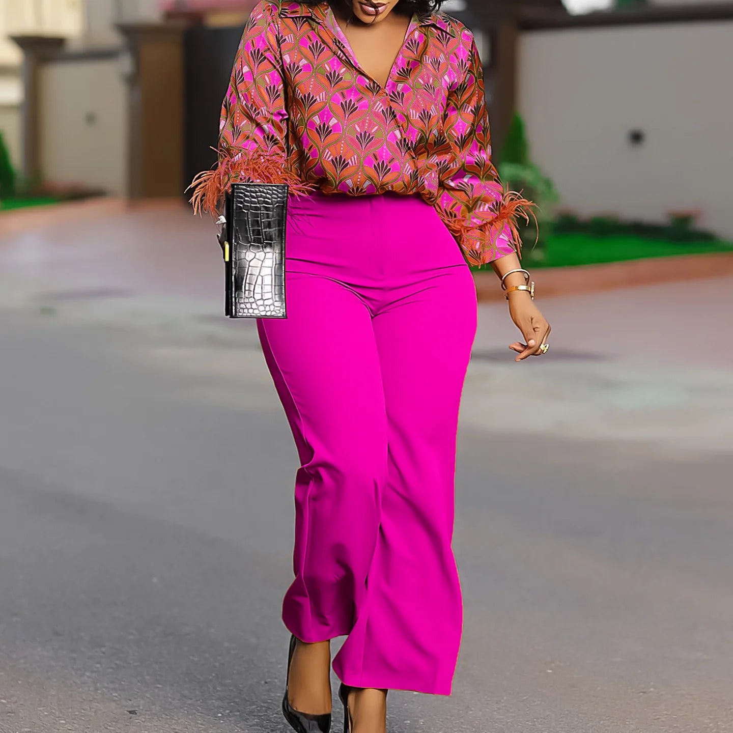 Woman in a colorful top and bright pink pants walking outdoors. African print two-piece polyester outfit with satin printed shirt and high waist wide leg pants. Comfortable, elegant office wear for women.