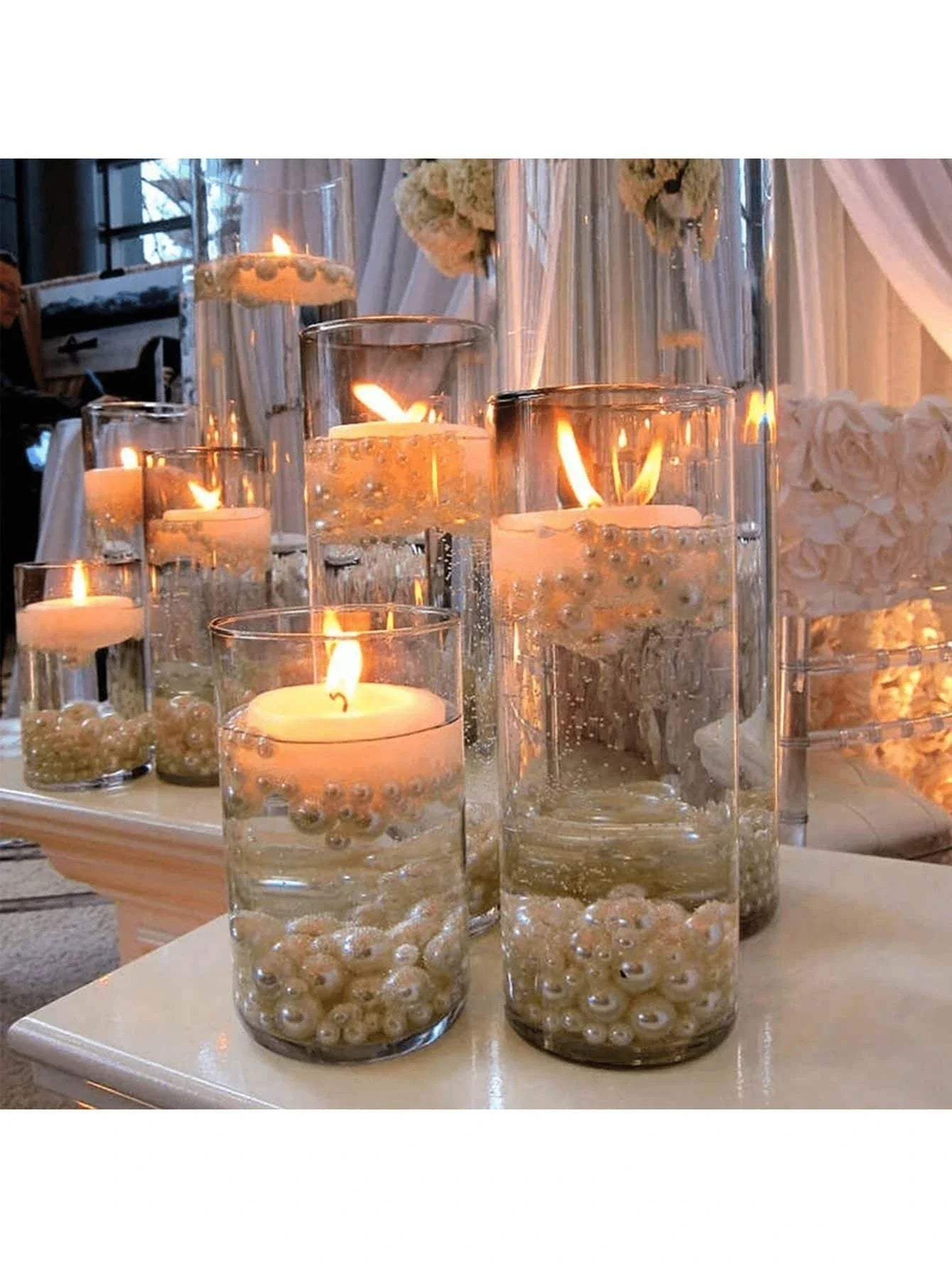 Decorative candles in glass holders with pearls on a table.
