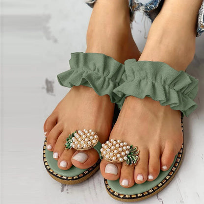 Green sandals with ruffled straps and decorative pineapple embellishments on a light background