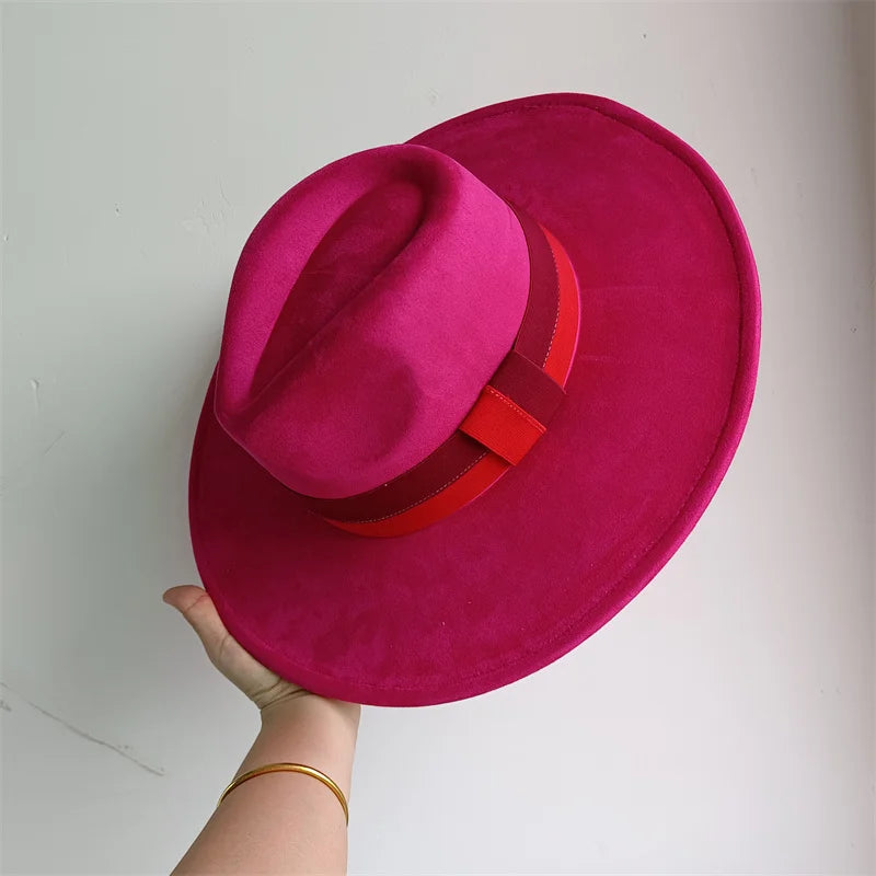 Pink hat with a red band held by a hand against a white background