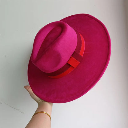 Pink hat with a red band held by a hand against a white background