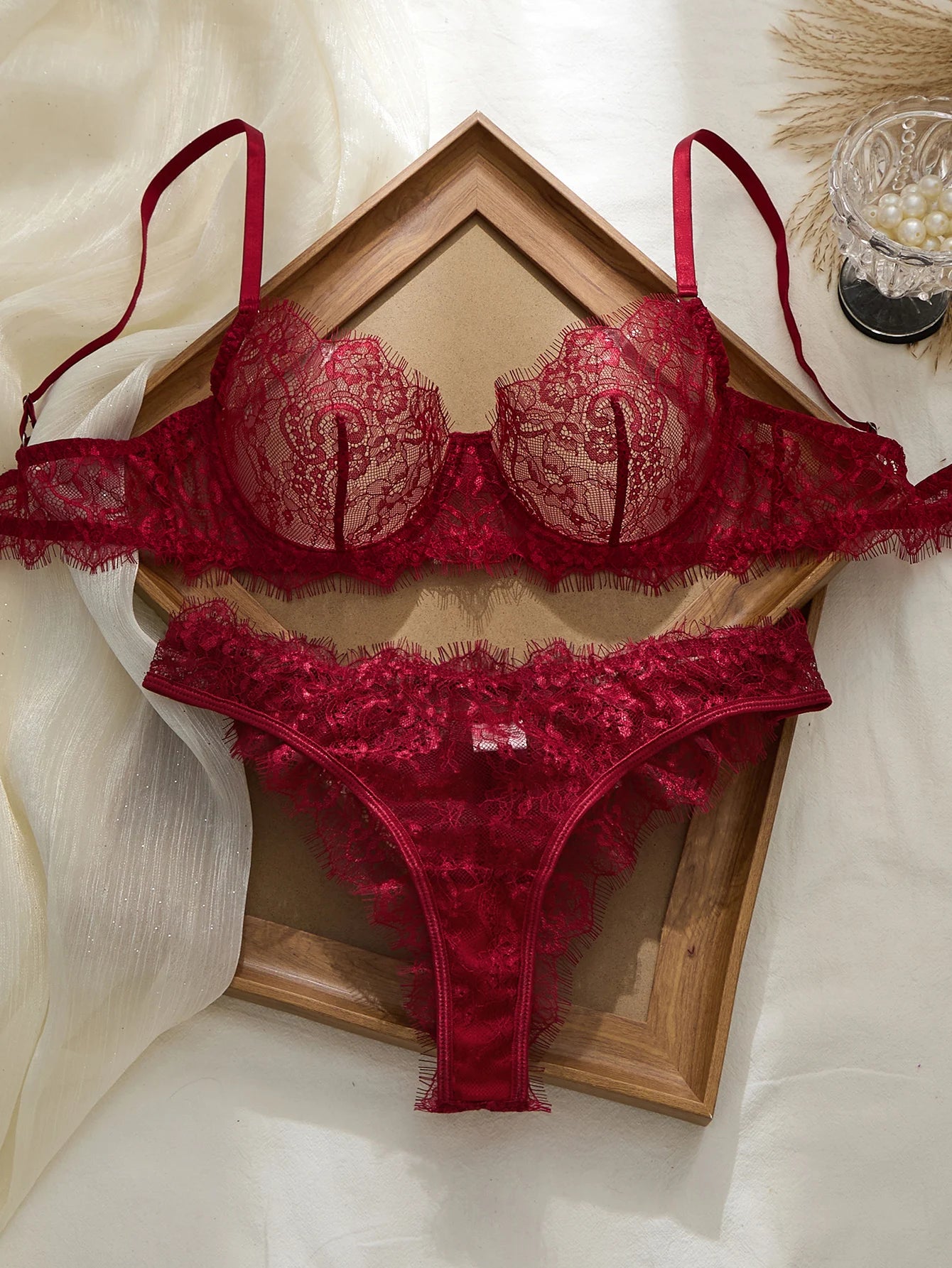 Red lace lingerie set on a wooden tray with a soft white background