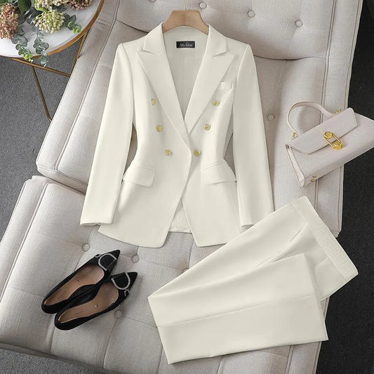 White suit with gold buttons on a white chair, accompanied by black shoes and a white handbag.