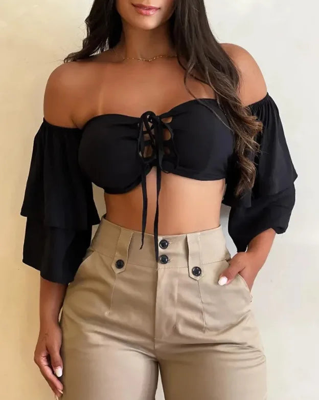 Woman wearing a black off-shoulder top and beige pants against a plain background