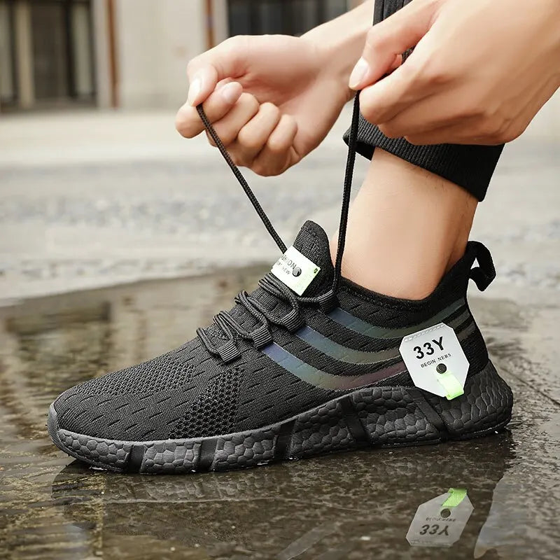 Person tying the laces of a black athletic shoe on a wet pavement.