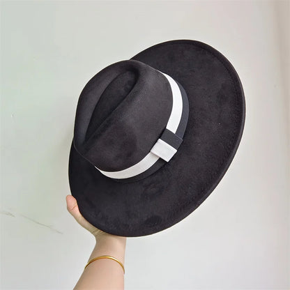 Black fedora hat with a white band held by a hand against a light gray background