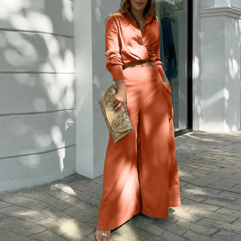 Person wearing an orange outfit standing outdoors on a sunny day. Women's elegant pants set with long sleeve crop shirt and high waist wide leg trousers. Office lady style. Solid, flattering, comfortable fit.