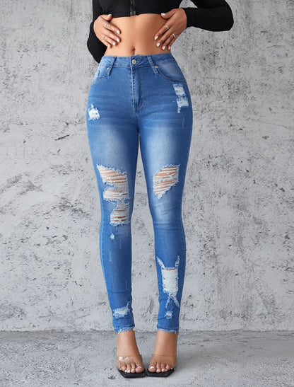 Blue distressed jeans worn by a person against a gray concrete wall. Women’s high waist ankle length skinny jeans, ripped and distressed, pockets, solid slim pencil fit. Vintage streetwear by ftf fashion UK.