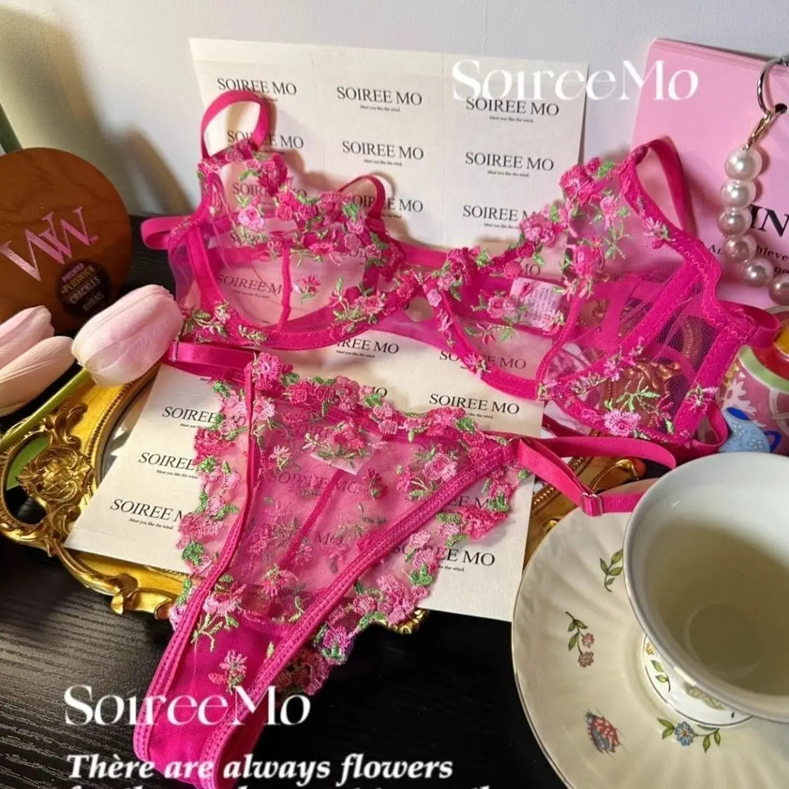 Pink floral lingerie set with 'SourceMo' branding on a table with a cup and saucer.