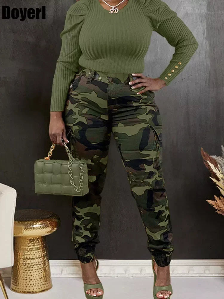 Woman in green top and camouflage pants holding a green handbag against a dark background