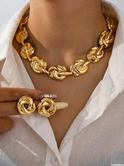 Woman in white shirt wearing gold knot chain statement necklace and round stud earrings