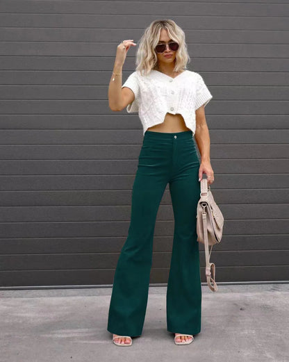 Woman wearing a white cropped top and green flared pants against a gray wall. Slim micro flare corduroy trousers with elastic waistband, screw thread button detail, casual style for women. Available in multiple colors UK FTF Market.