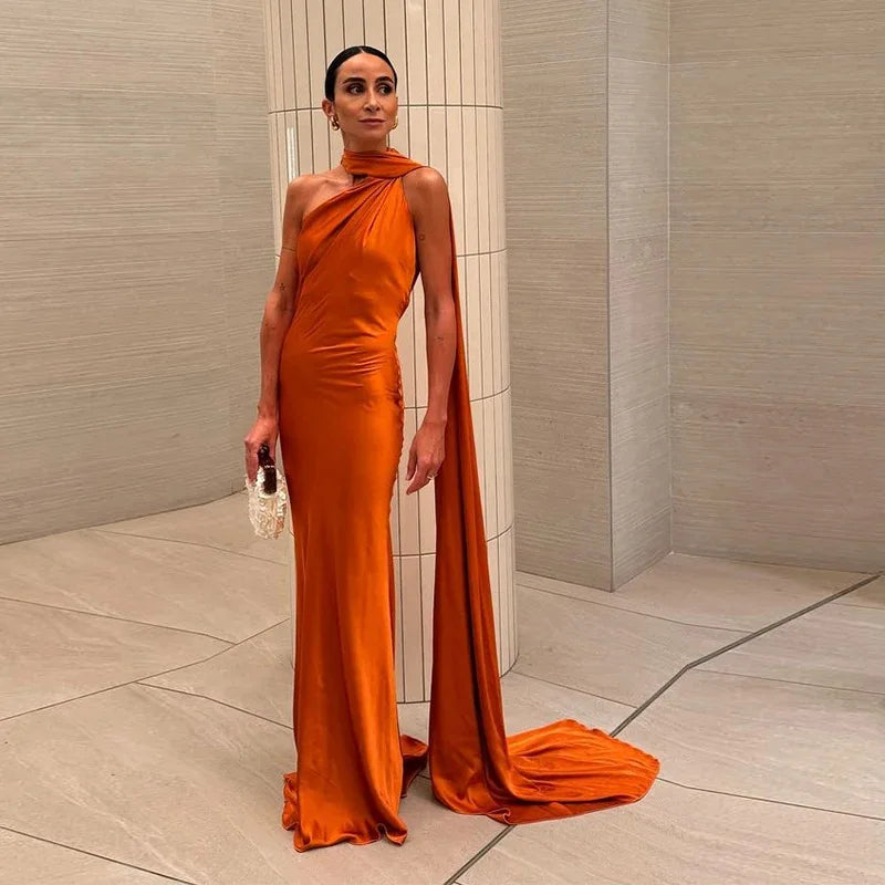 Woman in an orange evening gown standing against a neutral wall.