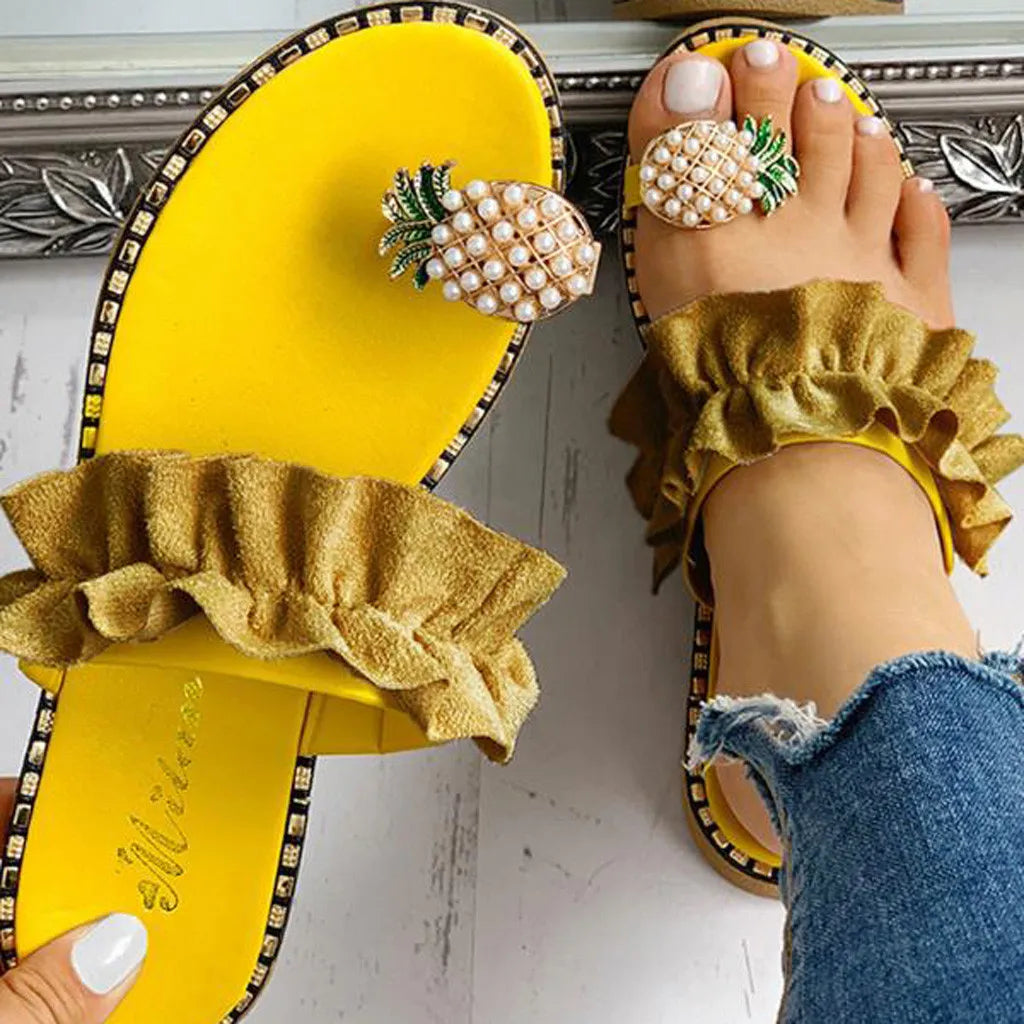 Yellow sandals with pineapple decorations worn by a person with blue jeans.
