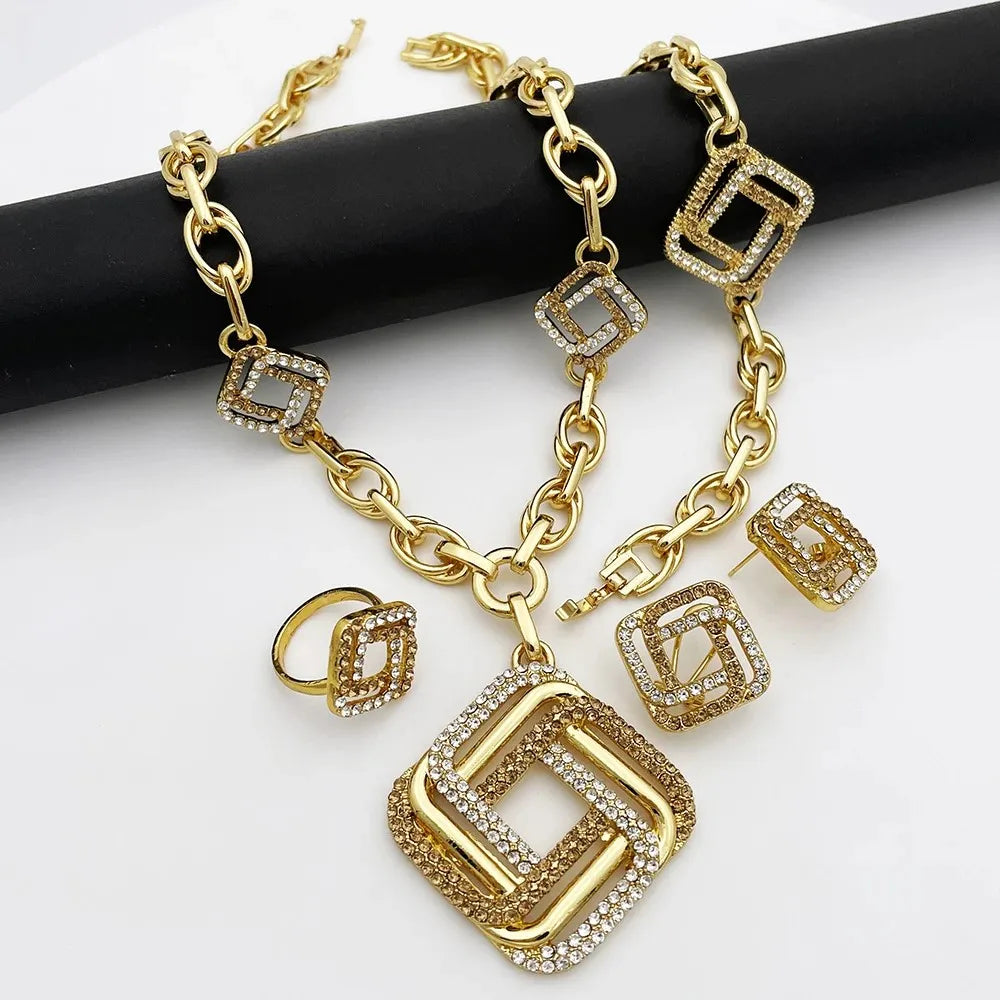 Gold-tone geometric chain necklace with matching stud earrings and a ring, featuring square links and clear rhinestone accents, displayed on a black cylindrical prop against a white background.