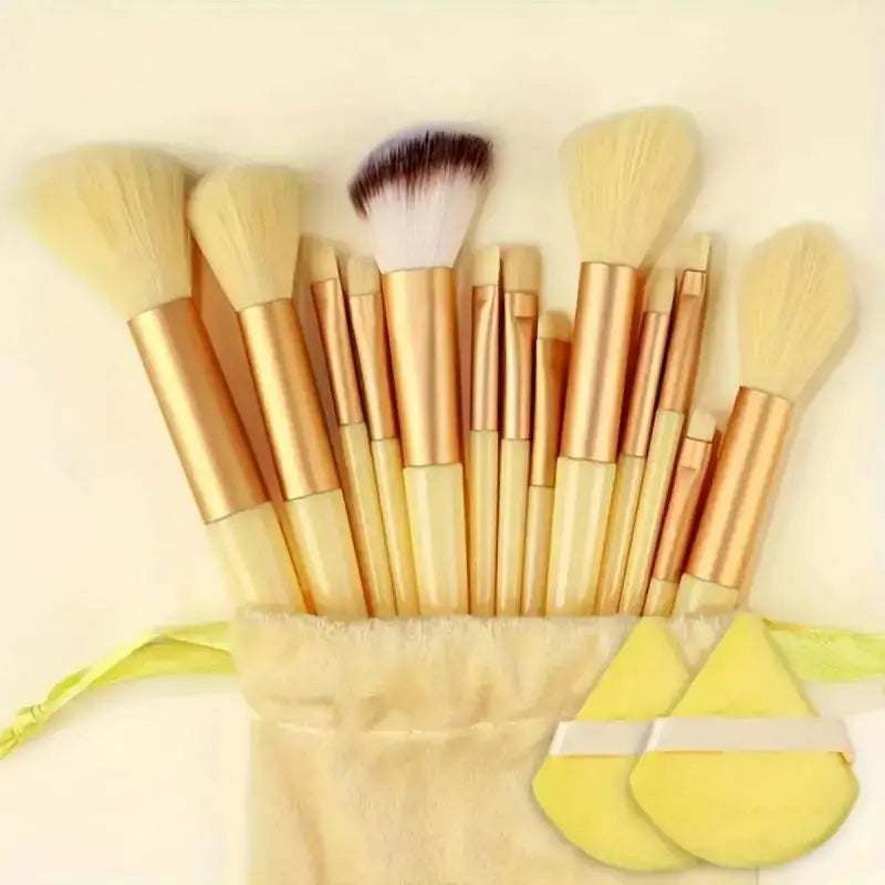 Set of gold makeup brushes with a yellow drawstring bag on a beige background. Soft fluffy makeup brush set with wool fiber bristles and plastic handles. Complete set for powder, foundation, eyeshadow, and beauty blending.
