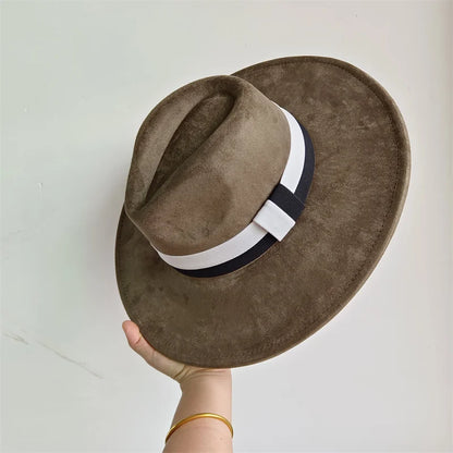 Brown fedora hat with a white and black band held against a light gray background