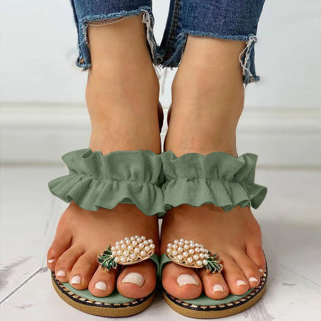 Green ruffled sandals with pearl embellishments worn by a person.
