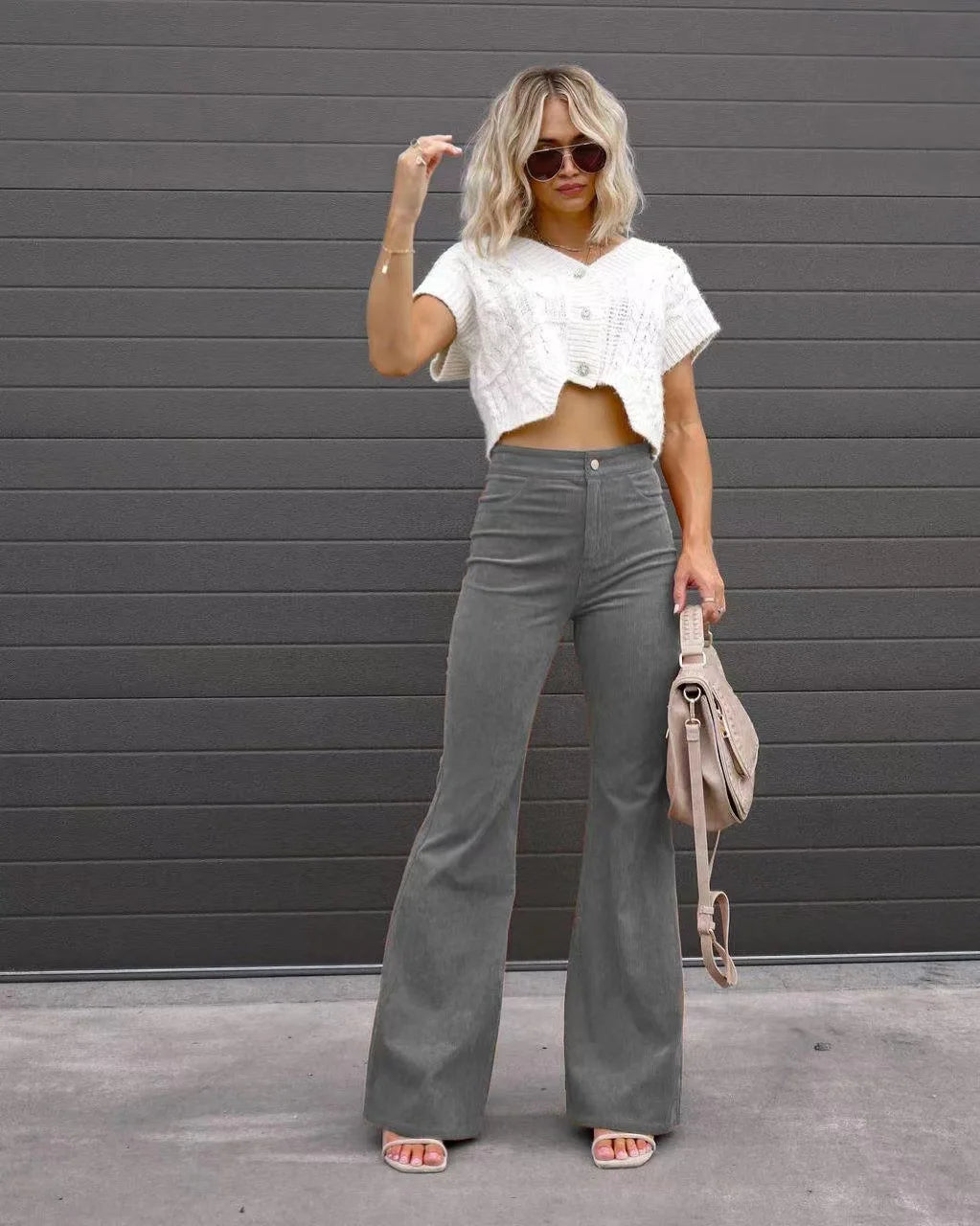Woman wearing a white cropped top and gray flared pants against a gray wall. Slim micro flare corduroy trousers with elastic waistband, screw thread button detail, casual style for women. Available in multiple colors UK FTF Market.