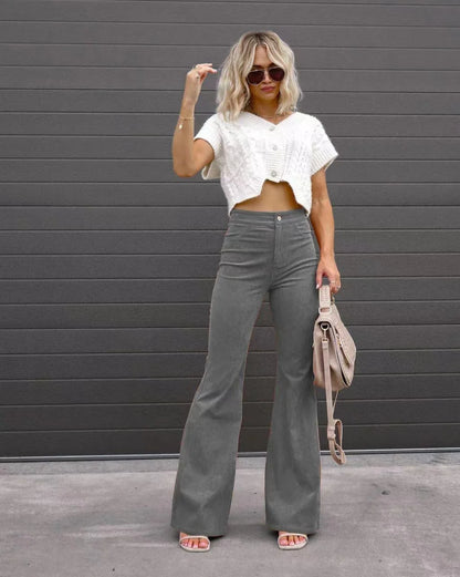 Woman wearing a white cropped top and gray flared pants against a gray wall. Slim micro flare corduroy trousers with elastic waistband, screw thread button detail, casual style for women. Available in multiple colors UK FTF Market.