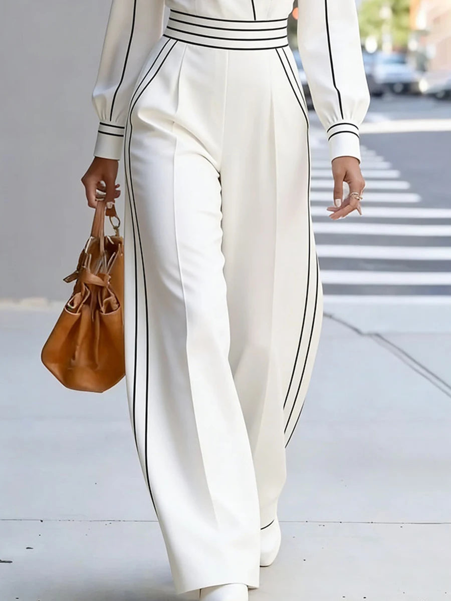 Person wearing a white outfit with black stripes, holding a brown handbag on a city street.