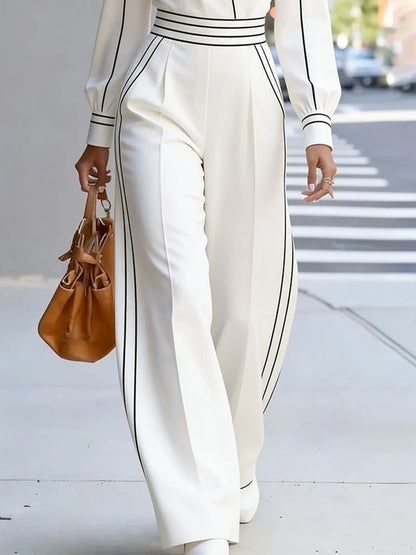 Person wearing a white outfit with black stripes, holding a brown handbag on a city street.