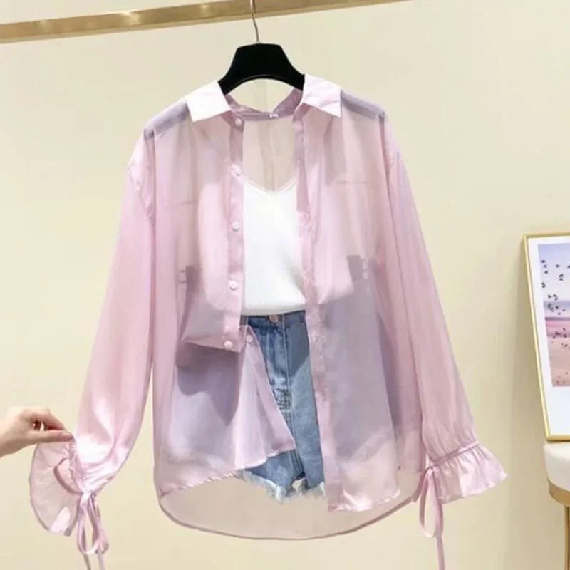 Pink sheer blouse over a white top and blue jeans on a hanger against a light background.