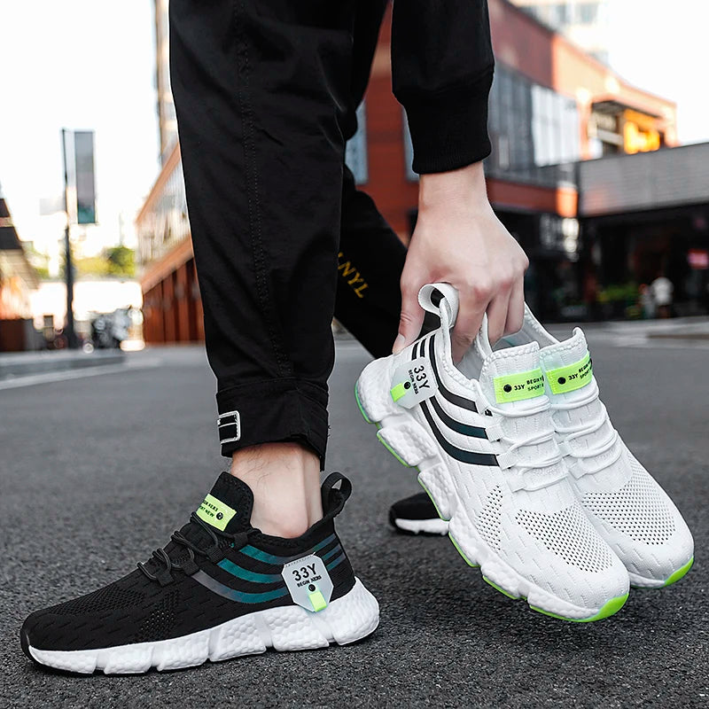 Person holding a pair of white sneakers with black and green accents on an urban street.