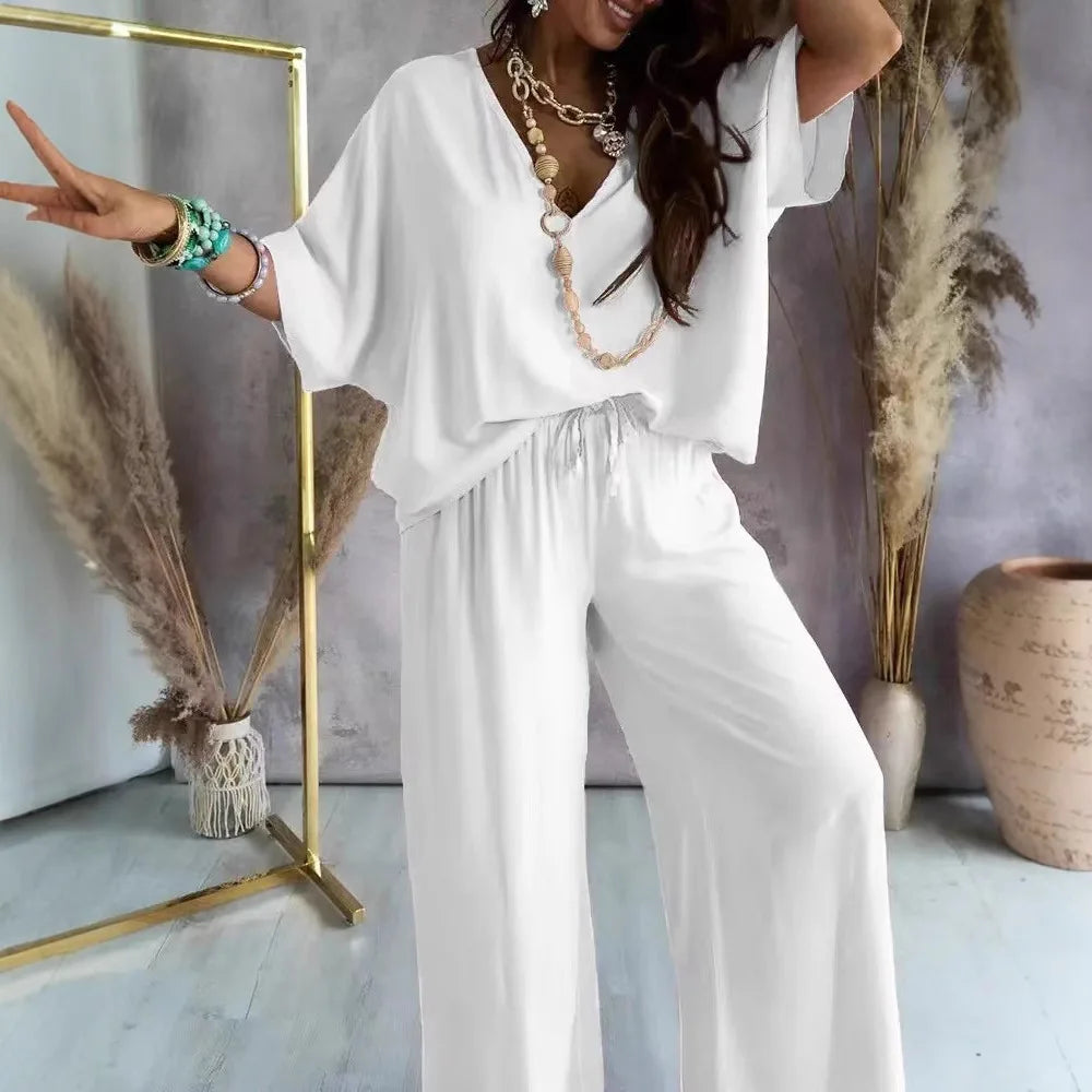 Woman in a white outfit posing in a stylish room with decor elements.