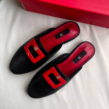 Black loafers with red buckles on a white surface