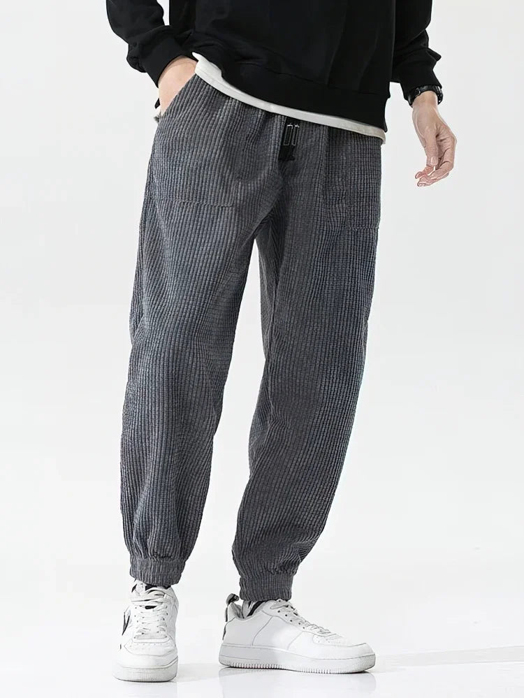 Person wearing gray checkered pants and white sneakers on a white background. Men's baggy corduroy jogger pants, tech fleece sweatpants, autumn winter harem trousers, elastic waist, thermal, UK FTF Market.