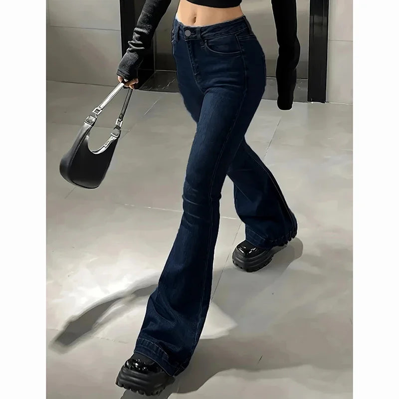 Person wearing dark blue flared jeans and black shoes, holding a black handbag. Women’s high waist flared jeans, stretchy bootcut denim trousers. Thin fabric, solid color, bell bottoms style for casual chic UK fashion.