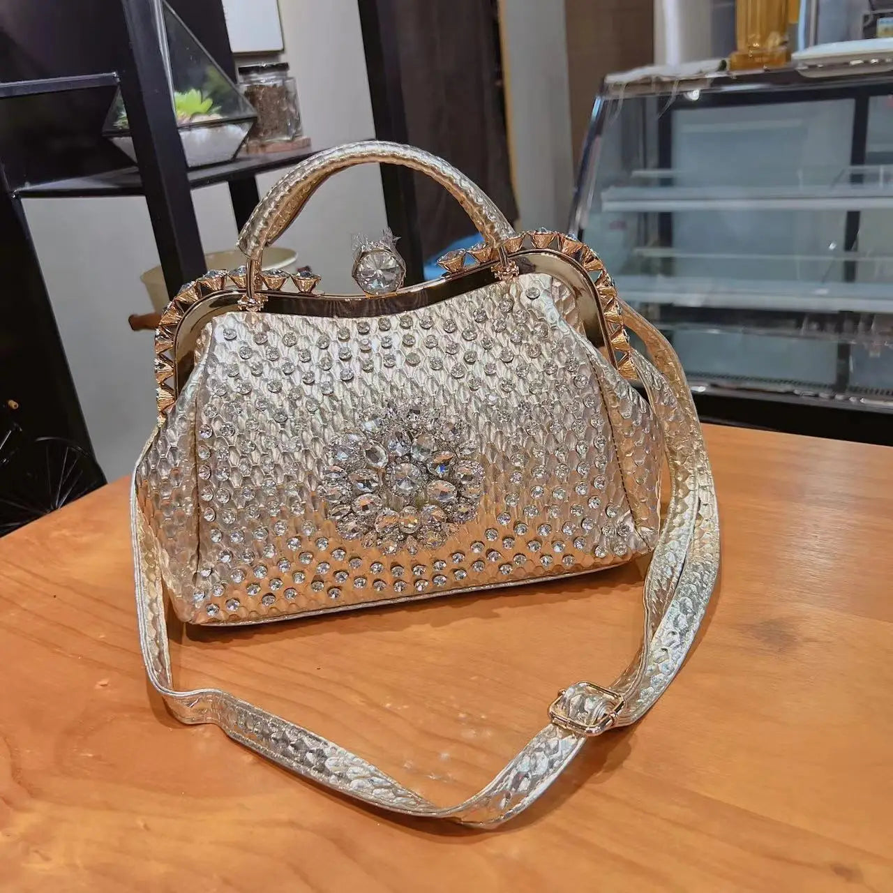Decorative handbag with rhinestone embellishments on a wooden surface. Large genuine leather dumpling bag with diamond rhinestone clip and lock clasp. Soft handle, multiple compartments. Fashionable shoulder tote for women.