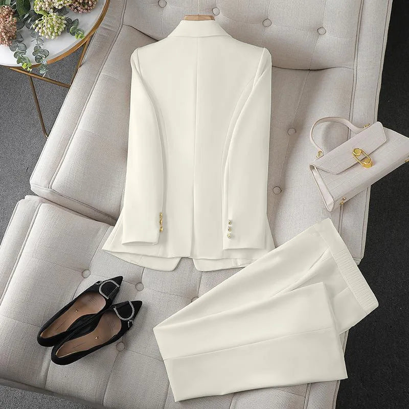White suit with gold buttons on a white chair, accompanied by black shoes and a white handbag.