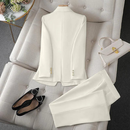 White suit with gold buttons on a white chair, accompanied by black shoes and a white handbag.