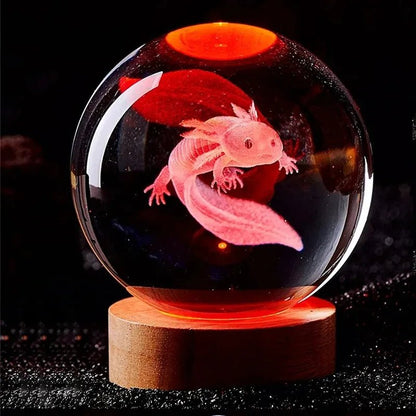 Pink axolotl inside a transparent sphere on a wooden base with a dark background. 3D laser engraved axolotl crystal ball lamp with USB LED base, vibrant colours UK.