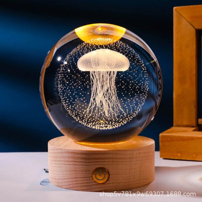 Glass orb with jellyfish design on a wooden base against a dark background. 3D laser engraved axolotl crystal ball lamp with USB LED base, vibrant colours UK.
