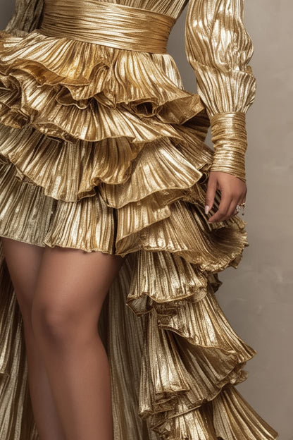 Close-up of a metallic gold ruffled dress with long sleeves and a dramatic layered skirt, shown on a model against a neutral beige background.