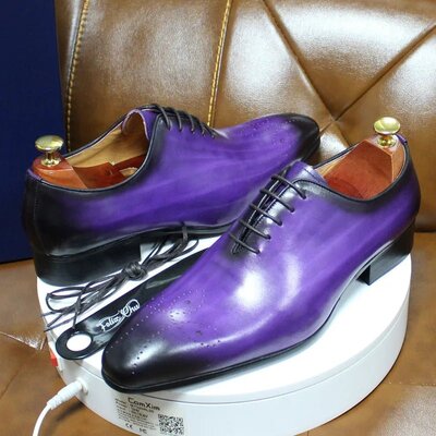 Purple and black dress shoes on a shoe tree with a brown leather chair in the background